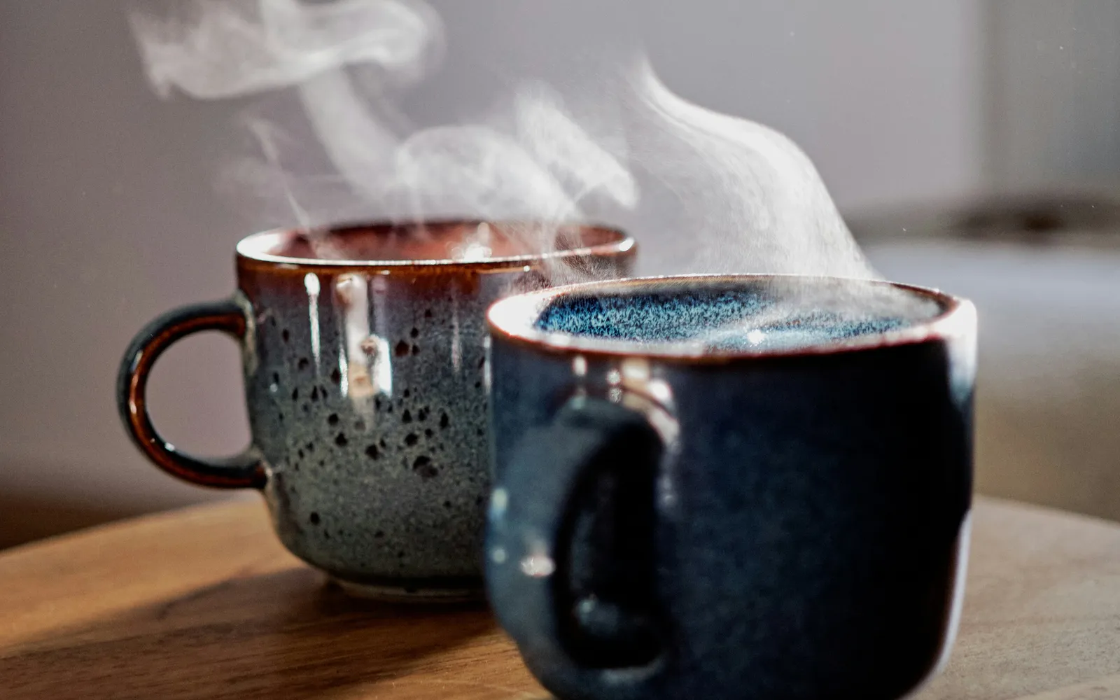 Deux tasses fumantes sur une table en bois, dans la lumière du matin