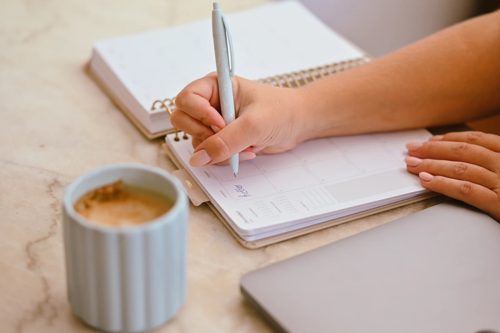 Une main écrit dans un agenda, à côté d’un café