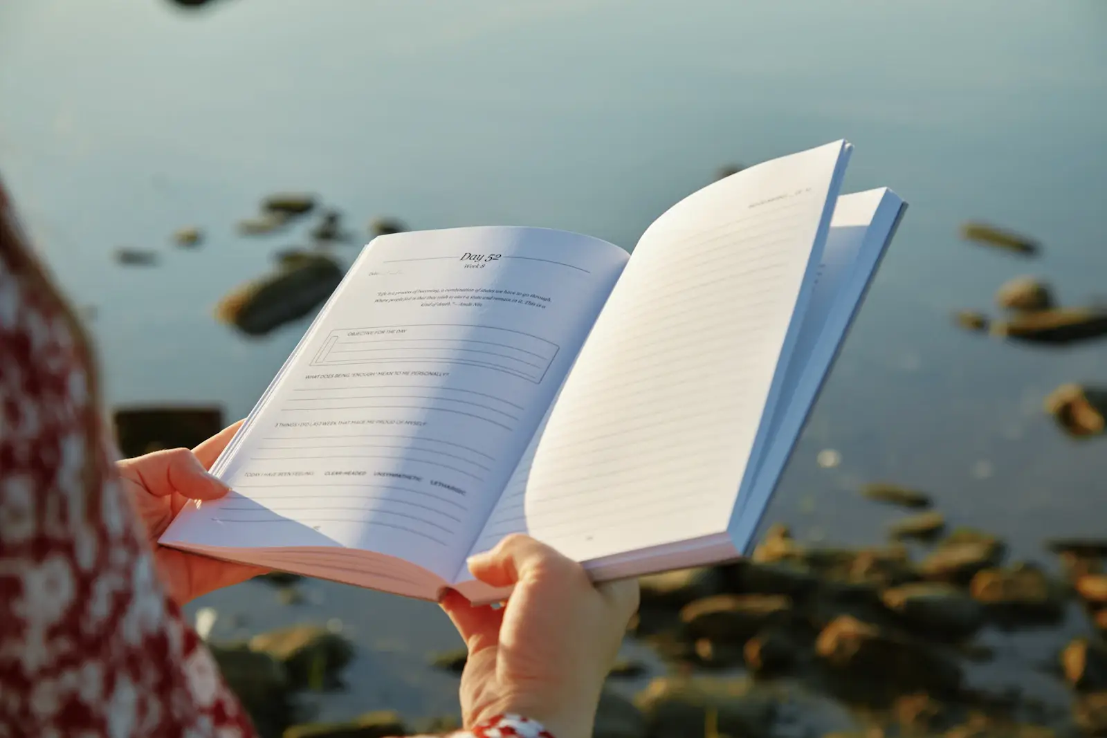 Des mains tenant un livre ouvert au bord de l’eau